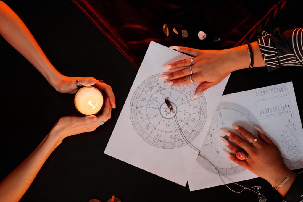 Astrology chart and candle on a dark table with two people’s hands, representing Astrodune’s astrologer community